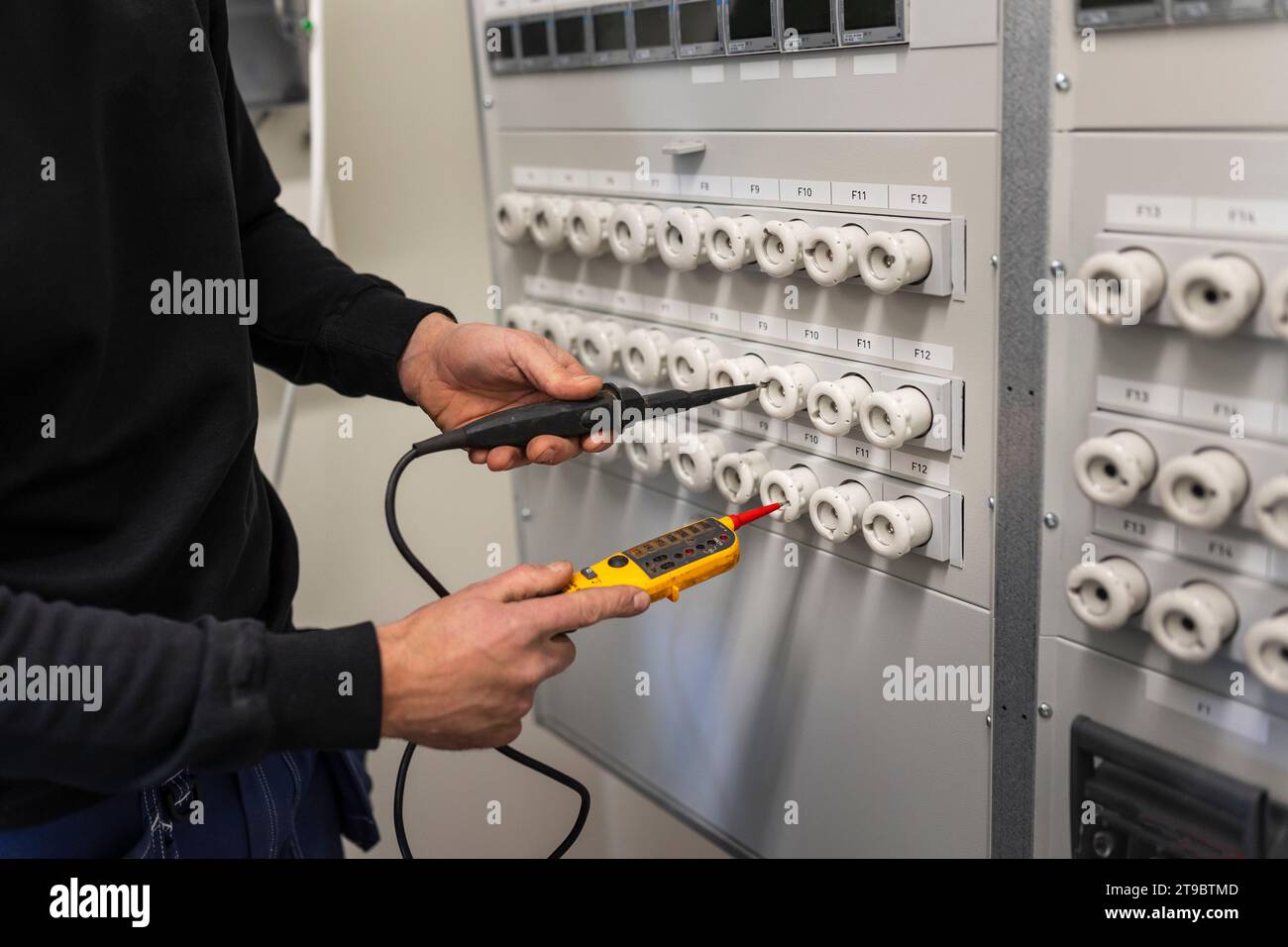 Mitte des männlichen Elektrikers mit Spannungsprüfer, der die Schalttafel im Zählerraum repariert Stockfoto