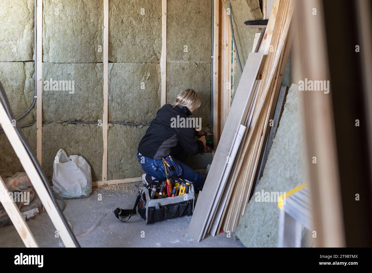 Weibliche Technikerin mit Bohrmaschine, die durch Werkzeugkasten an der Wand bohrt Stockfoto