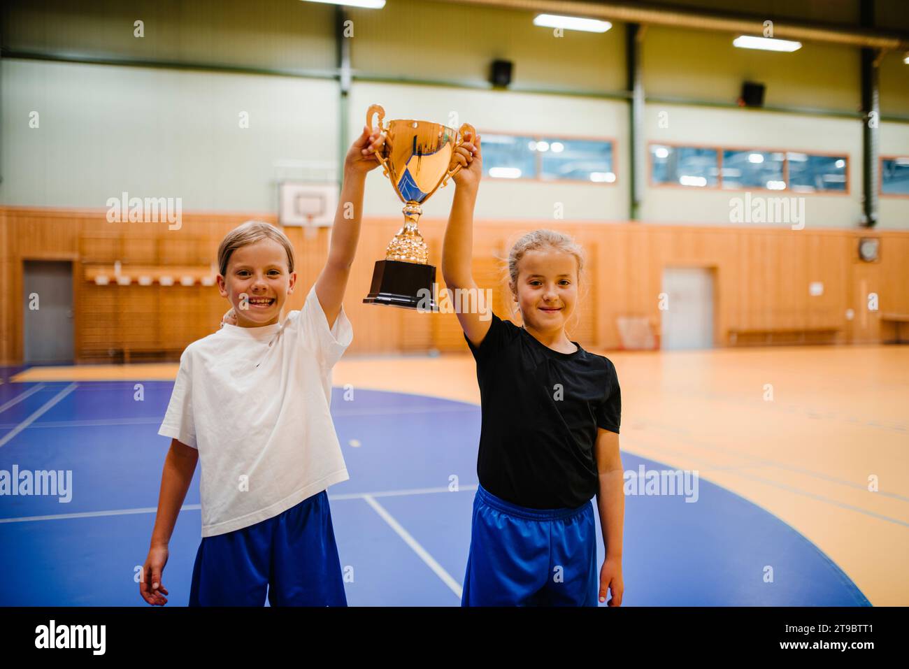Porträt glücklicher Spielerinnen mit Trophäe, während sie zusammen auf dem Sportplatz stehen Stockfoto