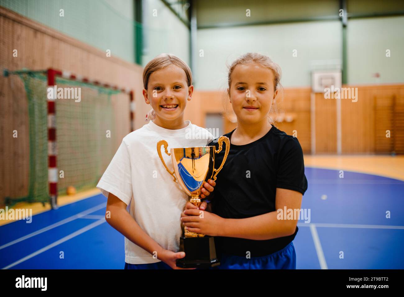 Porträt lächelnder Mädchen mit Trophäe beim gemeinsamen Stehen auf dem Sportplatz Stockfoto