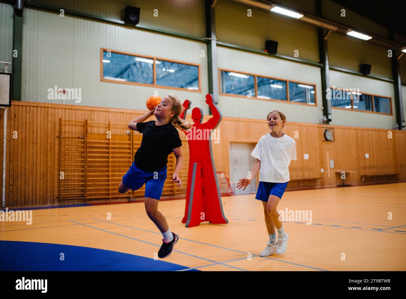 Ein Mädchen springt beim Handball mit einer Freundin auf dem Sportplatz Stockfoto