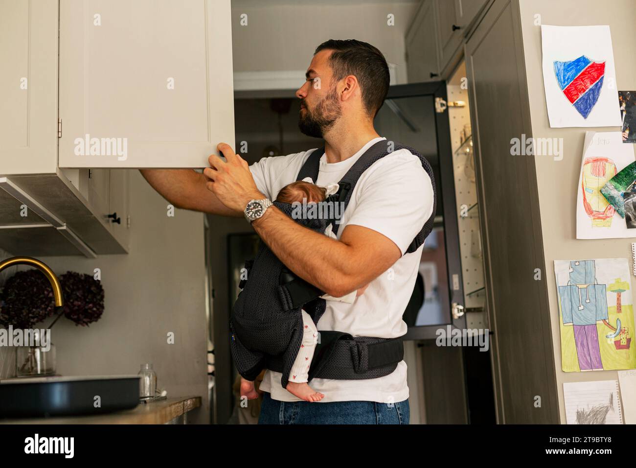 Vater öffnet den Schrank, während er den Sohn zu Hause in der Küche trägt Stockfoto