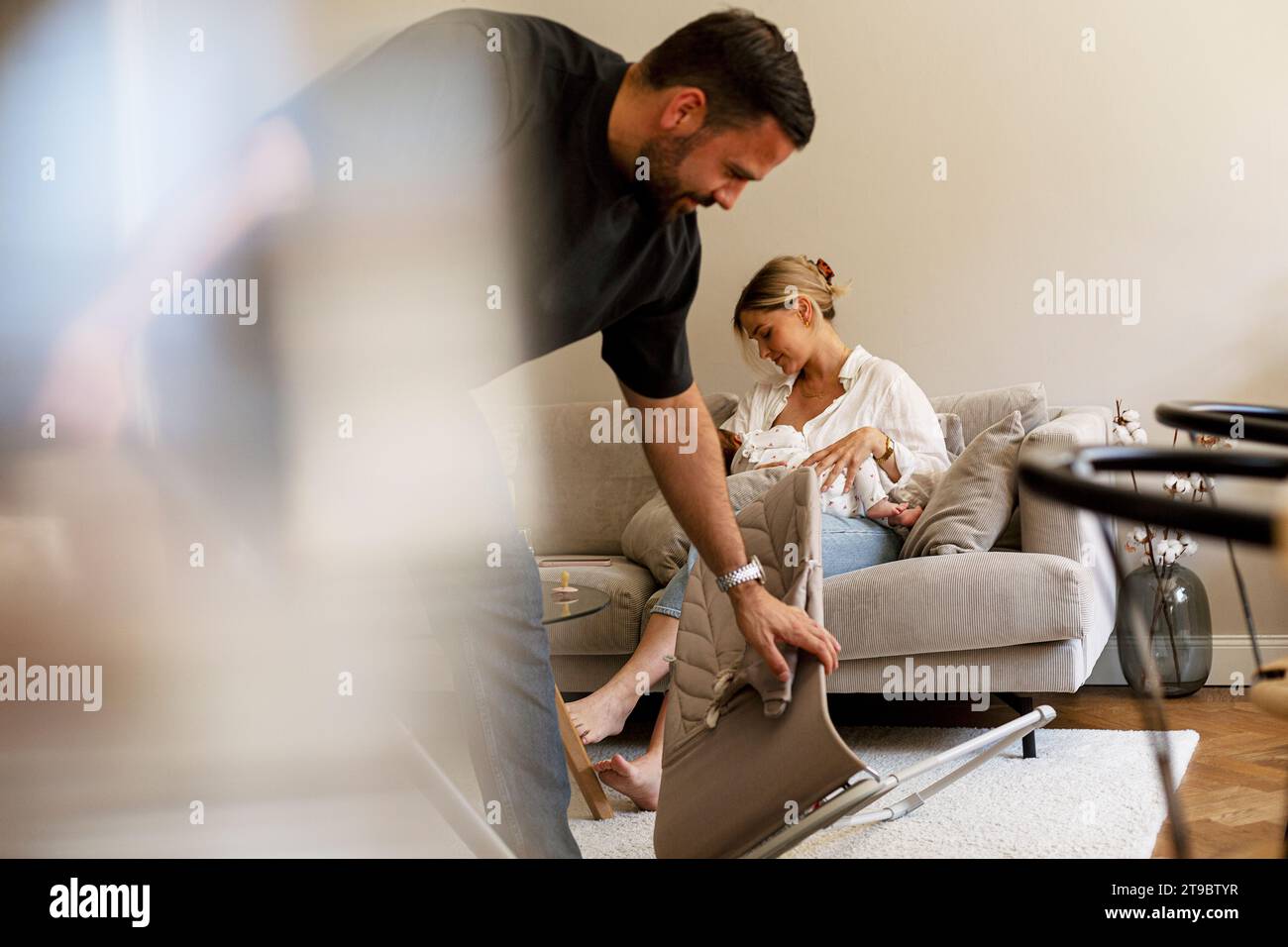 Vater putzt das Wohnzimmer, während Mutter zu Hause den Sohn stillt Stockfoto