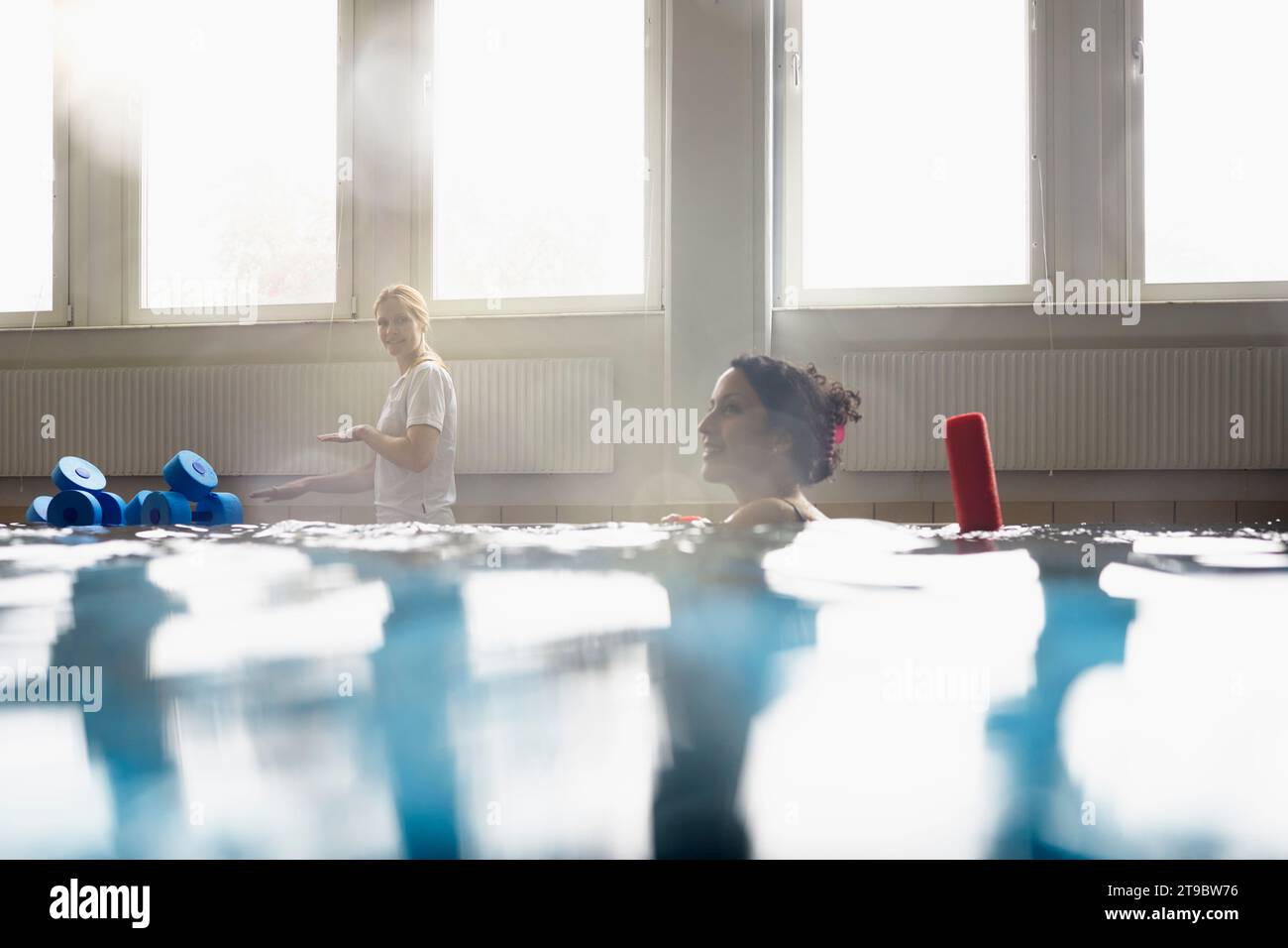 Lächelnde Frau mit Nudelschwaden im Schwimmbad im Rehabilitationszentrum Stockfoto