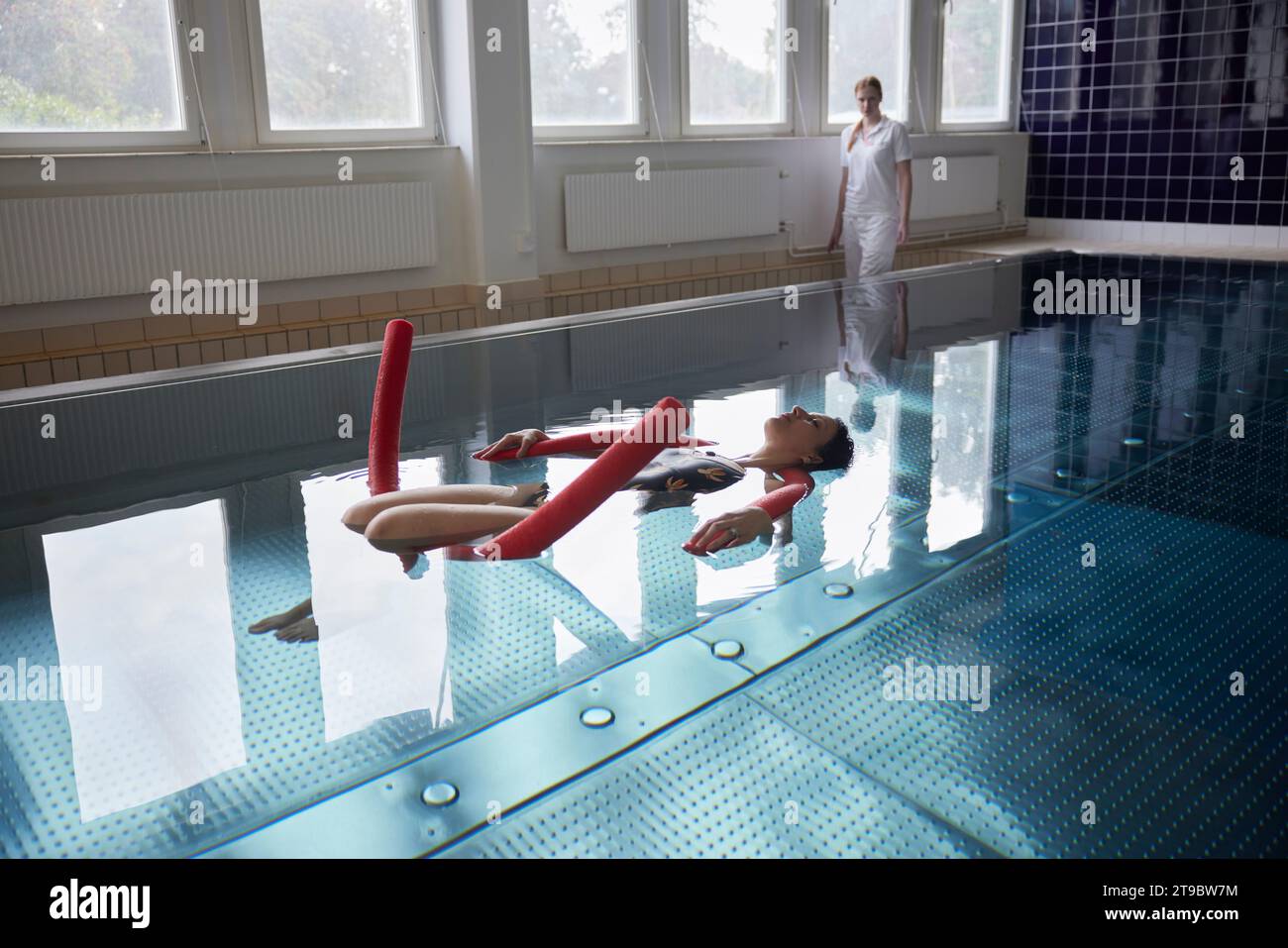 Die volle Länge einer Frau, die mit Nudelschwaden im Pool im Rehabilitationszentrum schwimmt Stockfoto