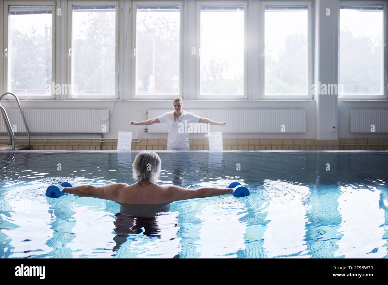Mann ohne Hemd, der mit Kurzhanteln im Schwimmbad im Rehabilitationszentrum trainiert Stockfoto