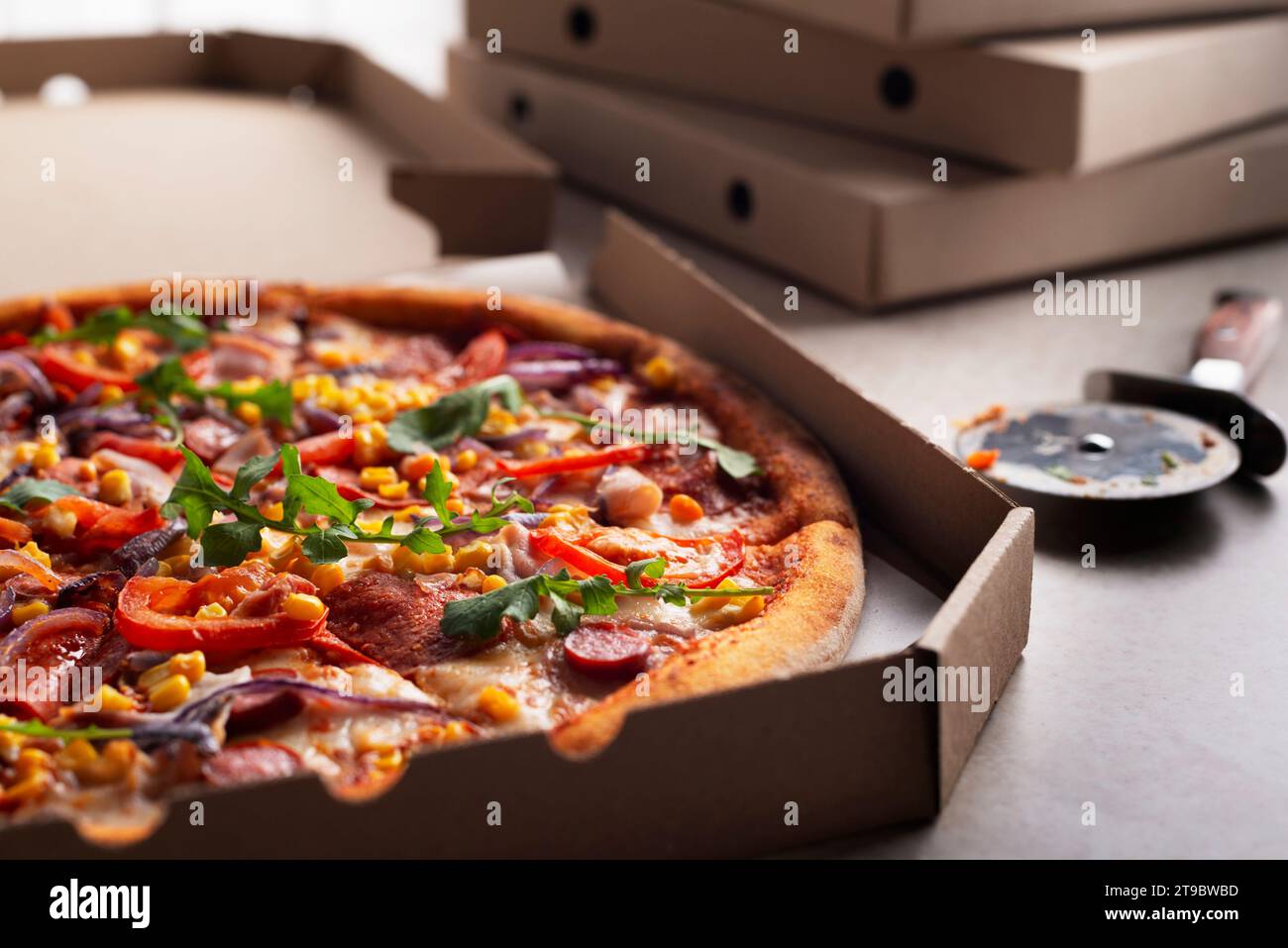 Große Pizza im offenen Karton und Cutter auf dem Küchentisch aus der Nähe Stockfoto