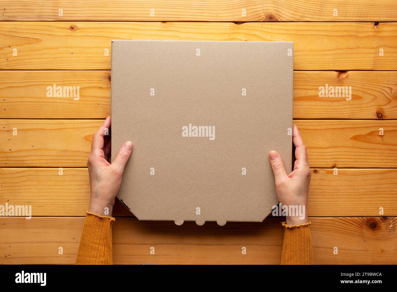 Pizza geschlossene Kartonbox in menschlichen kaukasischen Händen auf natürlichem Holztisch flach aufgelegtes Modell mit leerem Platz Stockfoto