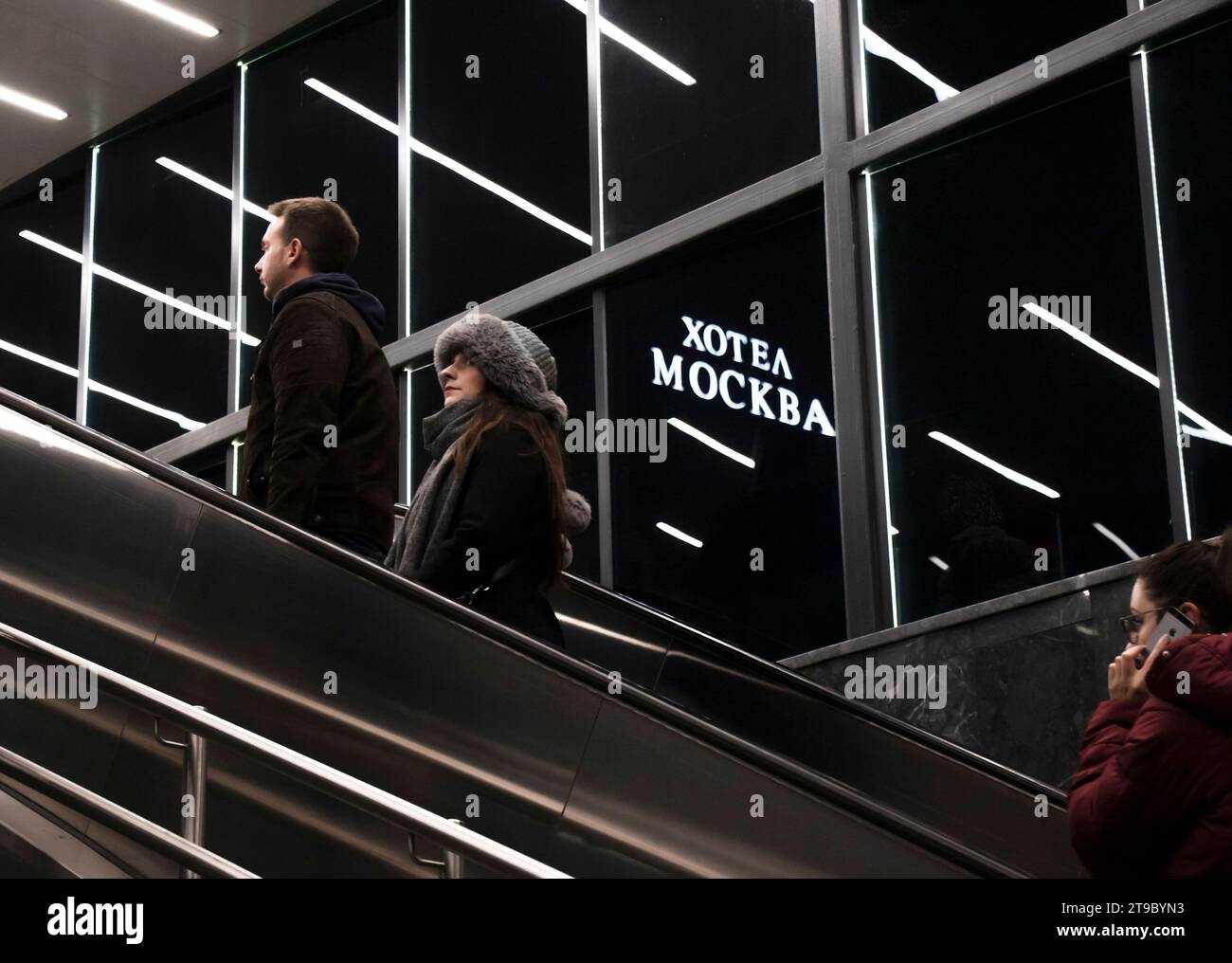 Belgrad, Serbien - 20. November 2023: Menschen, die die U-Bahn-Rolltreppe hinaufsteigen, mit reflektierender Innenbeleuchtung und Hotel Moskva-Schild in der Nacht Stockfoto