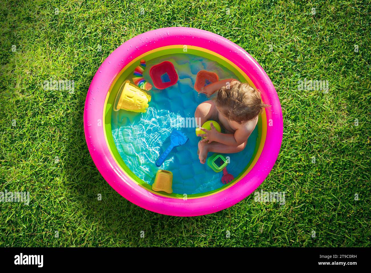 Junge, der in einem Pool im Garten sitzt und mit Wasserspielzeug spielt. Heißer Sommertag in der Natur Stockfoto