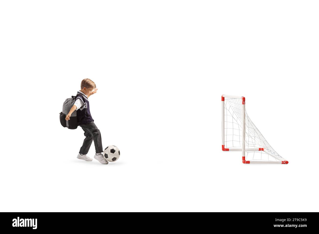 Schuljunge in Uniform, der einen Fußball auf Minitore auf weißem Hintergrund tritt Stockfoto