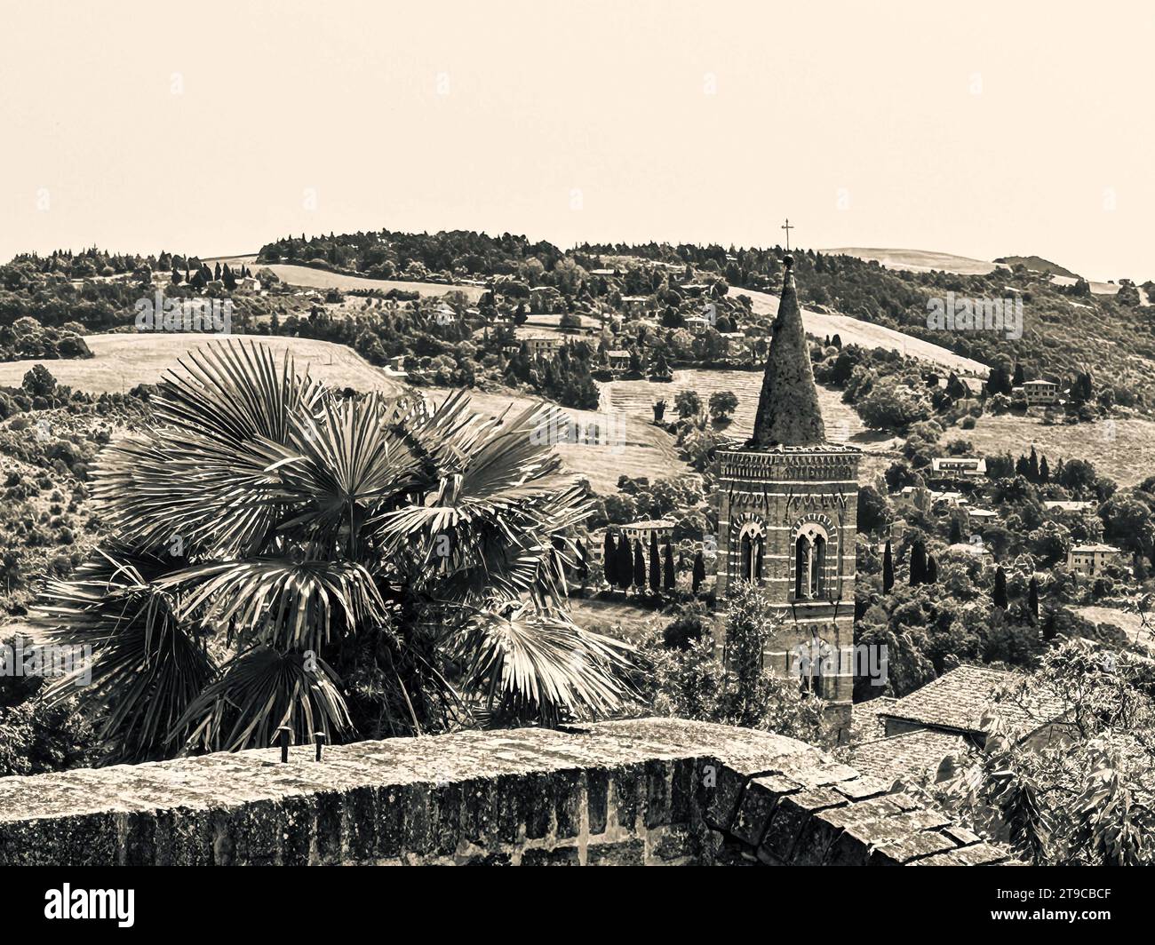 Heilige Ruhe trifft auf natürliche Pracht: Ein Kirchturm steht anmutig, geschmückt von einer sich wiegenden Palme im Vordergrund, während majestätische Berge pro Jahr Stockfoto