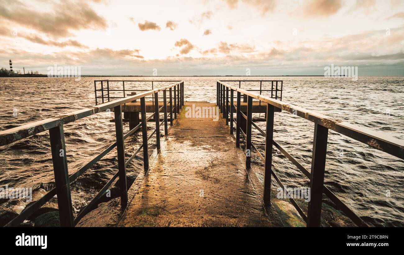 Bei Sonnenuntergang erstreckt sich das Metalldock mit seinen anmutigen Gliedmaßen über das Meer und wirft lange Schatten, die den ruhigen Tanz des verblassten Tages auf dem Wasser spiegeln Stockfoto