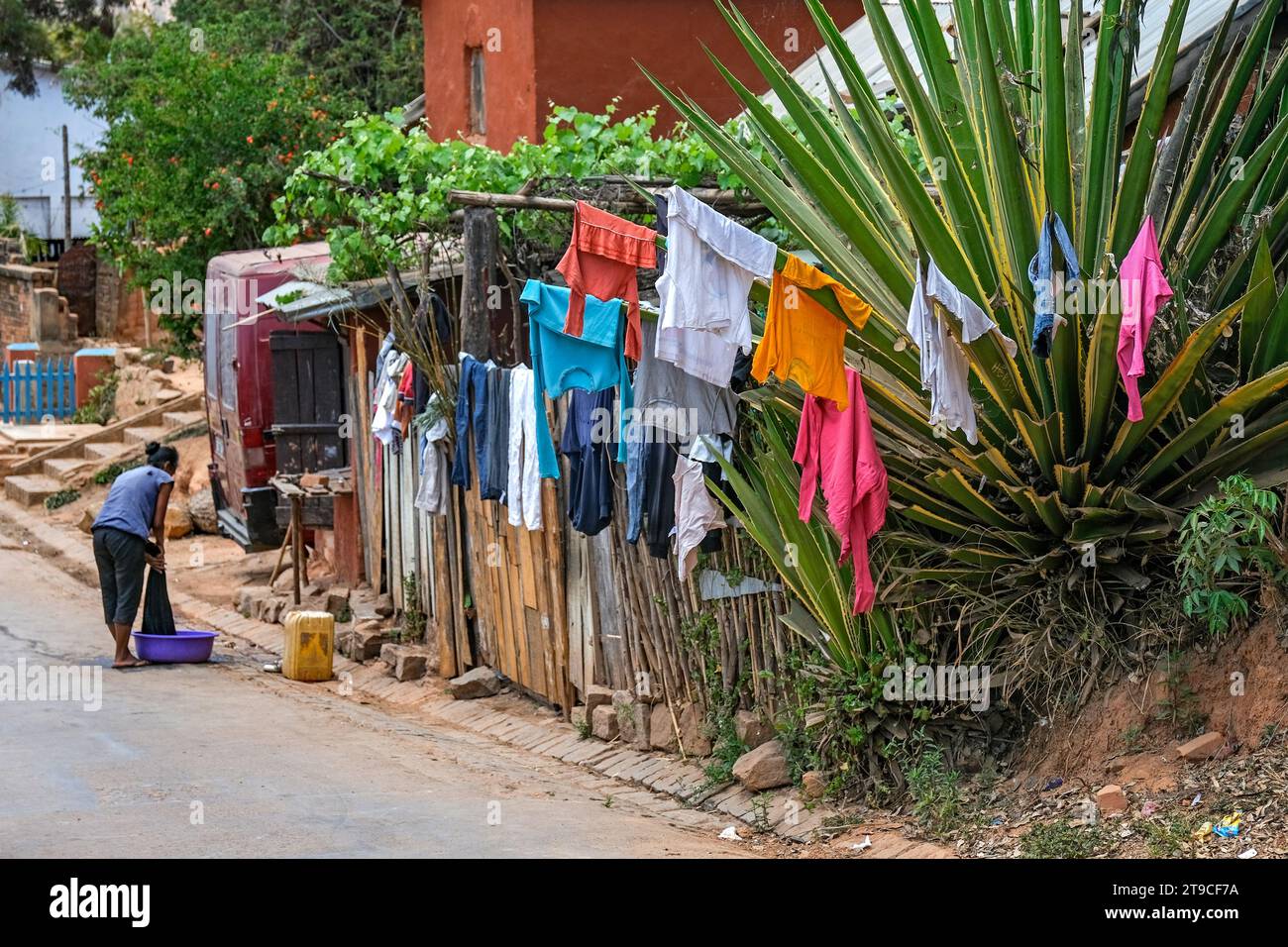 Madagassische Frau wäscht Kleidung auf der Straße und Wäsche hängt an saftigen Blättern im Dorf Ambohimanga Rova in der Nähe von Antananarivo, Madagaskar, Afrika Stockfoto