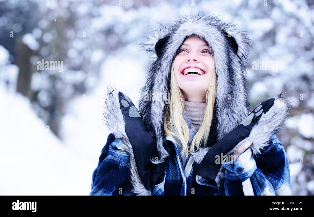 Winterferien und Urlaub. Glückliches blondes Mädchen spazieren im verschneiten Wald. Schöne Frau im karierten Mantel, Pelzmütze und Fäustlinge im Winterpark. Weihnachten Stockfoto