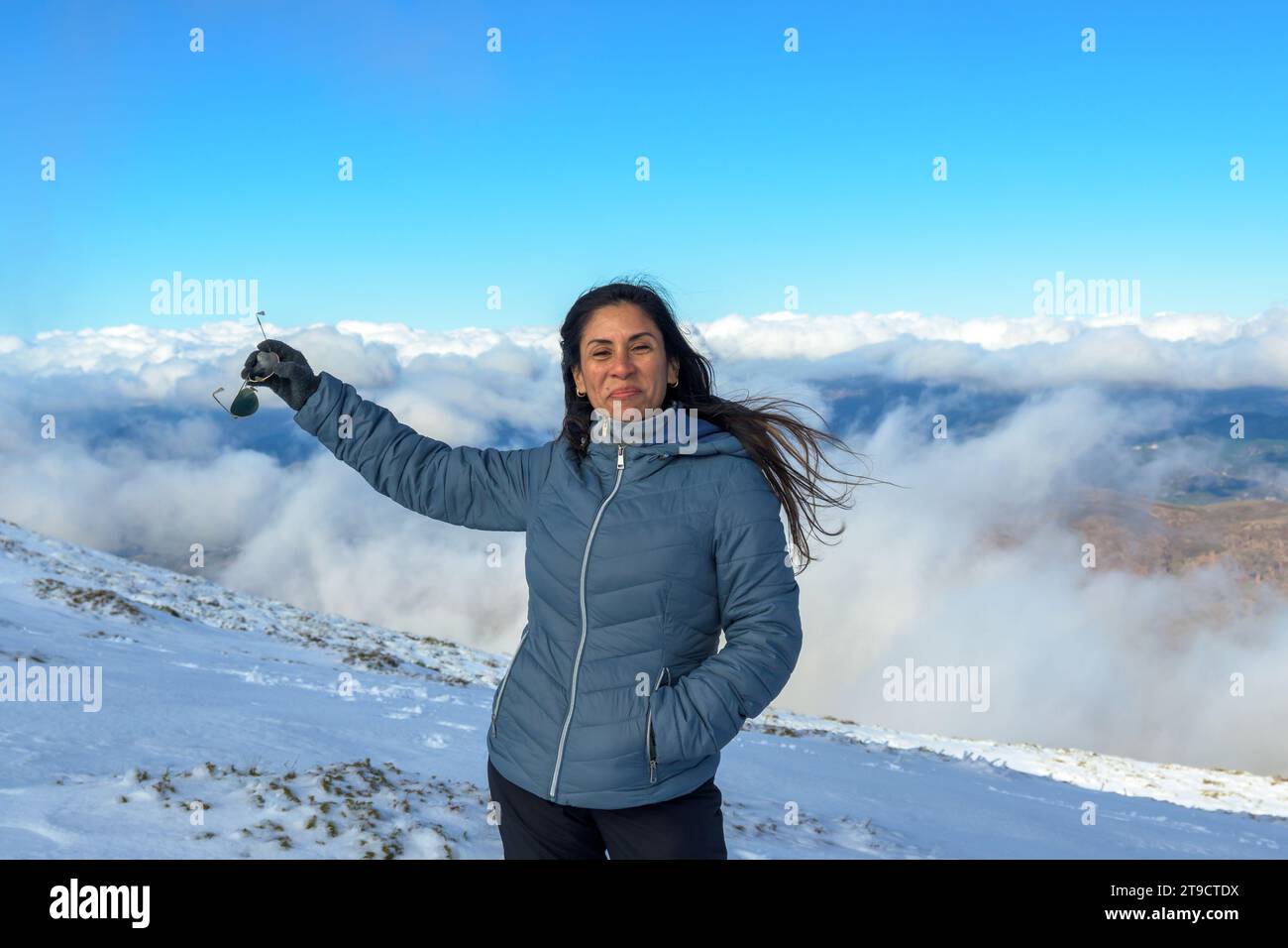 Porträt einer lateinischen Frau, die im Schnee lächelt, mit warmen Kleidern über den Wolken, auf dem Gipfel des Berges der sierra nevada Stockfoto