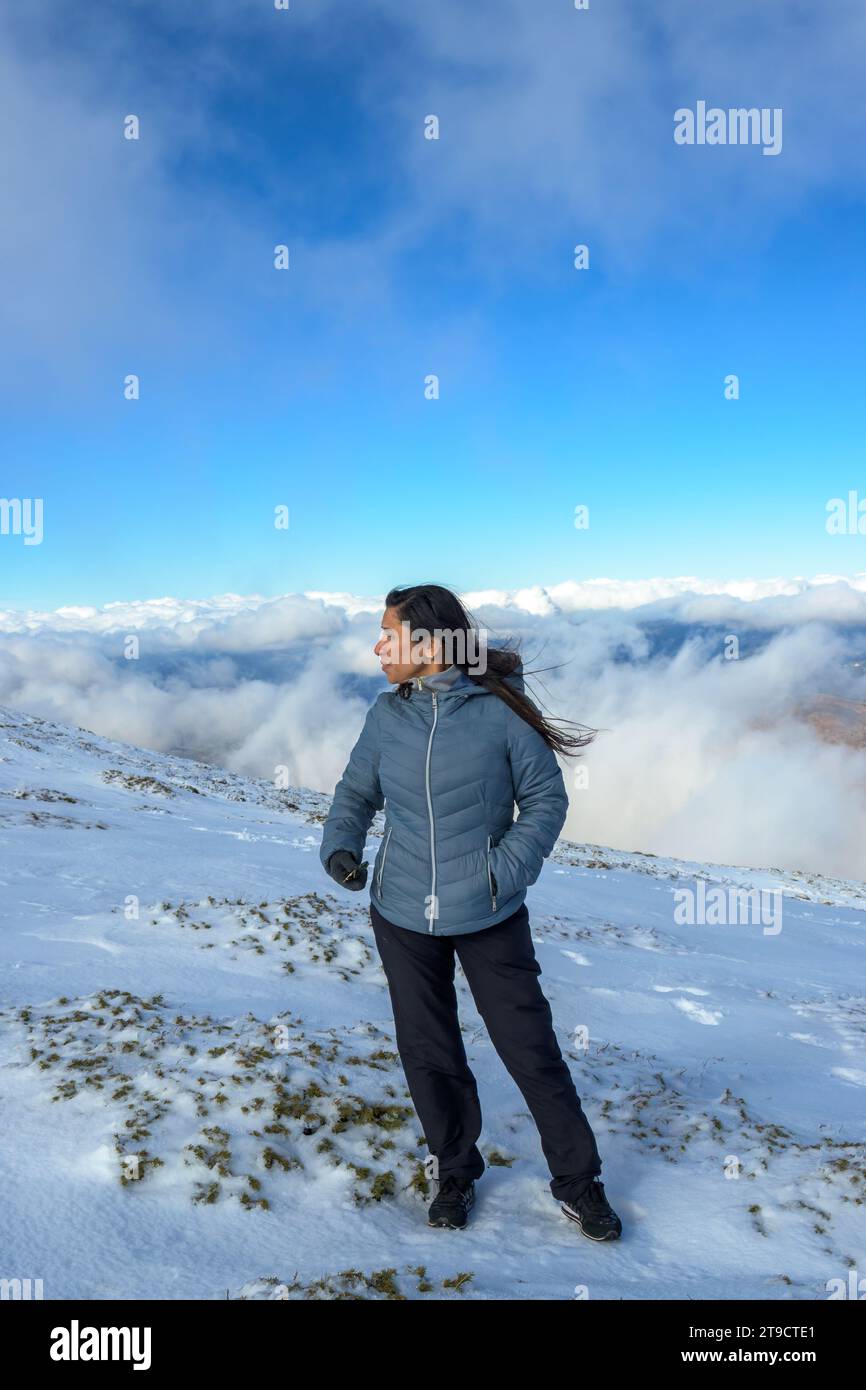 Latina-Frau mittleren Alters auf einem schneebedeckten Berg über den Wolken, Stockfoto