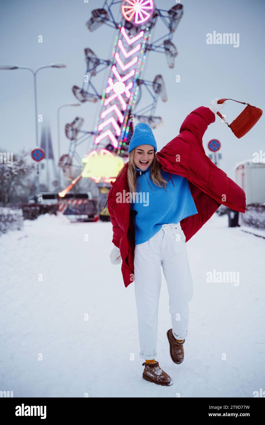 Die fröhliche und stilvolle Frau in warmen Kleidern macht Spaß in einem verschneiten Winterspazierpark. Stockfoto