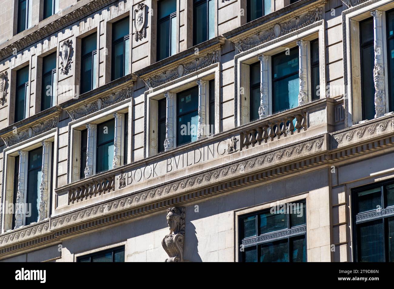 Die Inschrift „Book Building“ schmückt das Gesims der historistischen Fassade des Book Building im Zentrum von Detroit, Michigan, USA, wobei eine Steinstatue mit einer Fackel über dem Eingang Wache hält. Erbaut 1917 nach Entwürfen des Architekten Louis Kamper im italienischen Renaissance-Stil, bildet das 13-stöckige Gebäude zusammen mit dem angrenzenden Book Tower, der 1926 fertiggestellt wurde und den das Immobilienunternehmen Bedrock 2023 nach einer siebenjährigen, rund 300 Millionen Dollar teuren Restaurierung wiedereröffnete, einen Komplex. Stockfoto