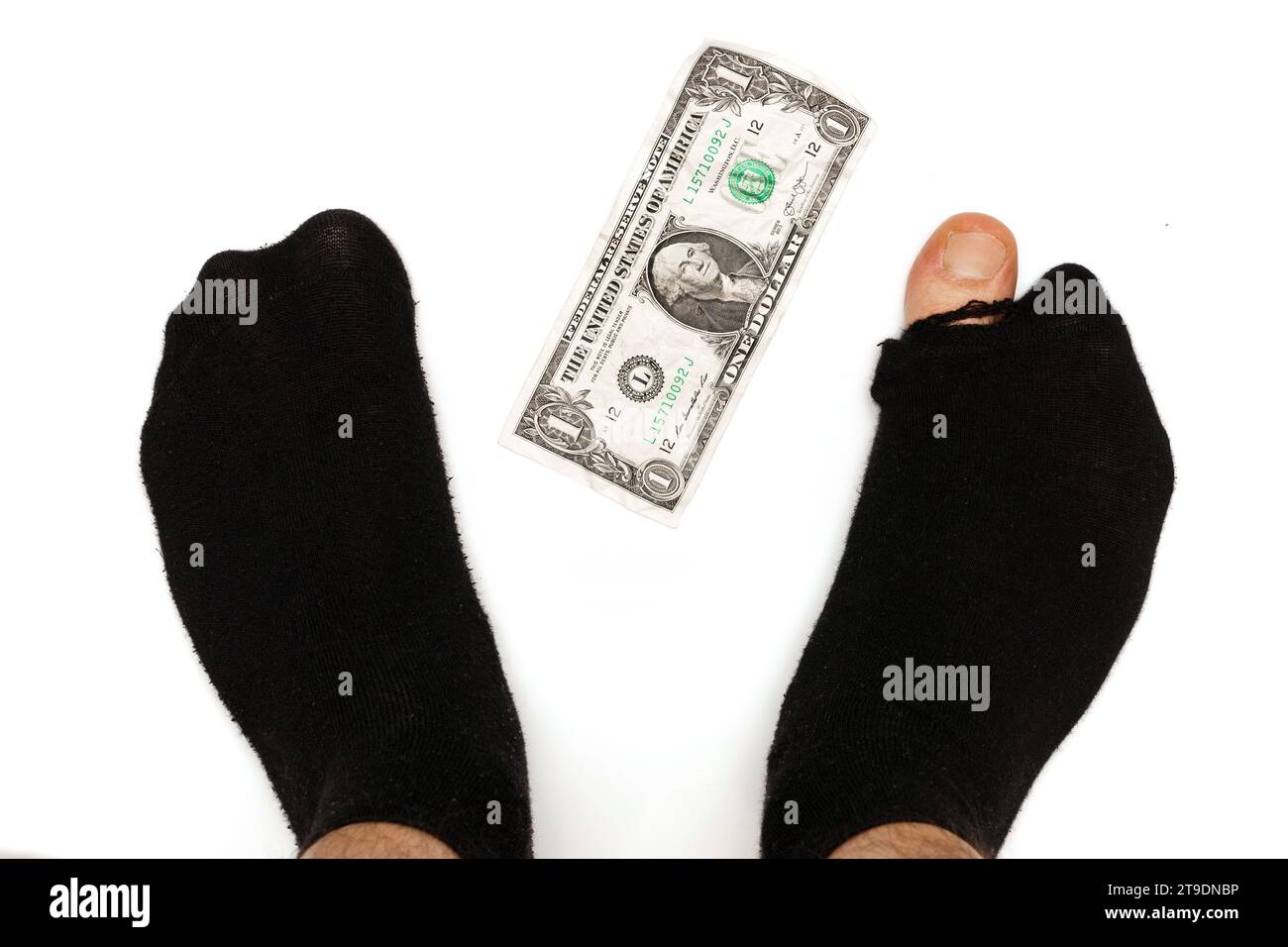Nahaufnahme eines männlichen Fußes in schwarzen Socken mit herausstehender Spitze und einer 1-Dollar-Banknote auf weißem Hintergrund. Armutsbegriff und Financi Stockfoto