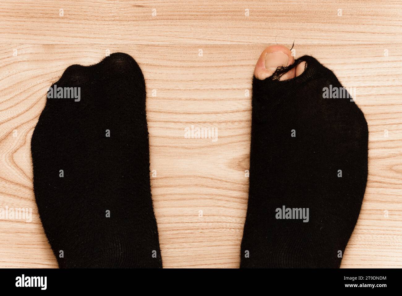Nahaufnahme von männlichen Füßen in alten Socken mit einem Zeh, der auf Holzboden steht. Konzept von Armut und Finanzkrise. Stockfoto