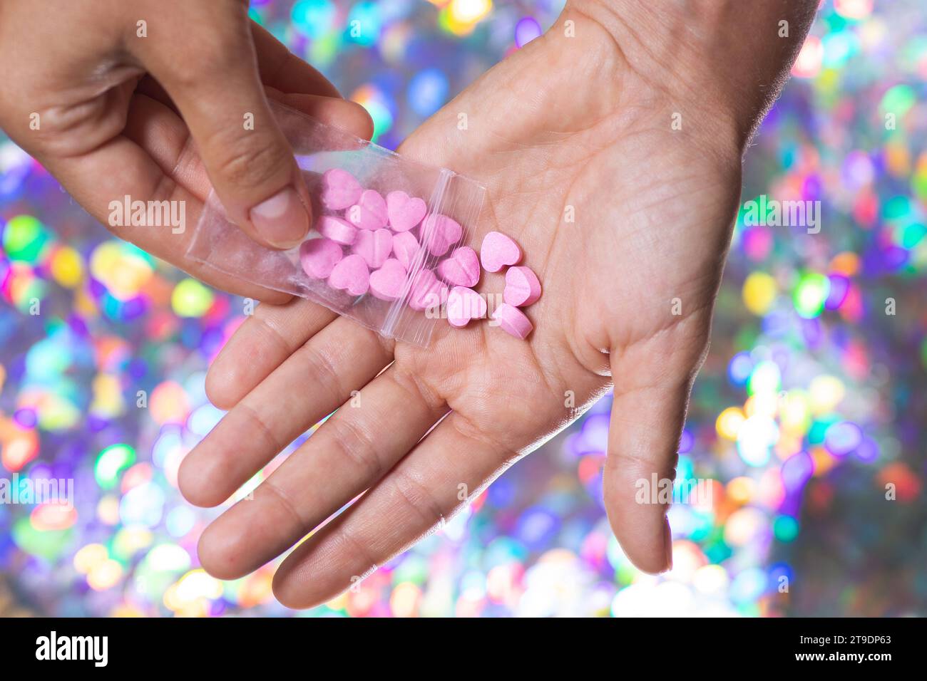 Nahaufnahme eines Mannes, der rosafarbene herzförmige Pillen auf seine Handfläche aus einem transparenten Reißverschlussbeutel auf hellem, unscharfem Hintergrund gießt. Stockfoto
