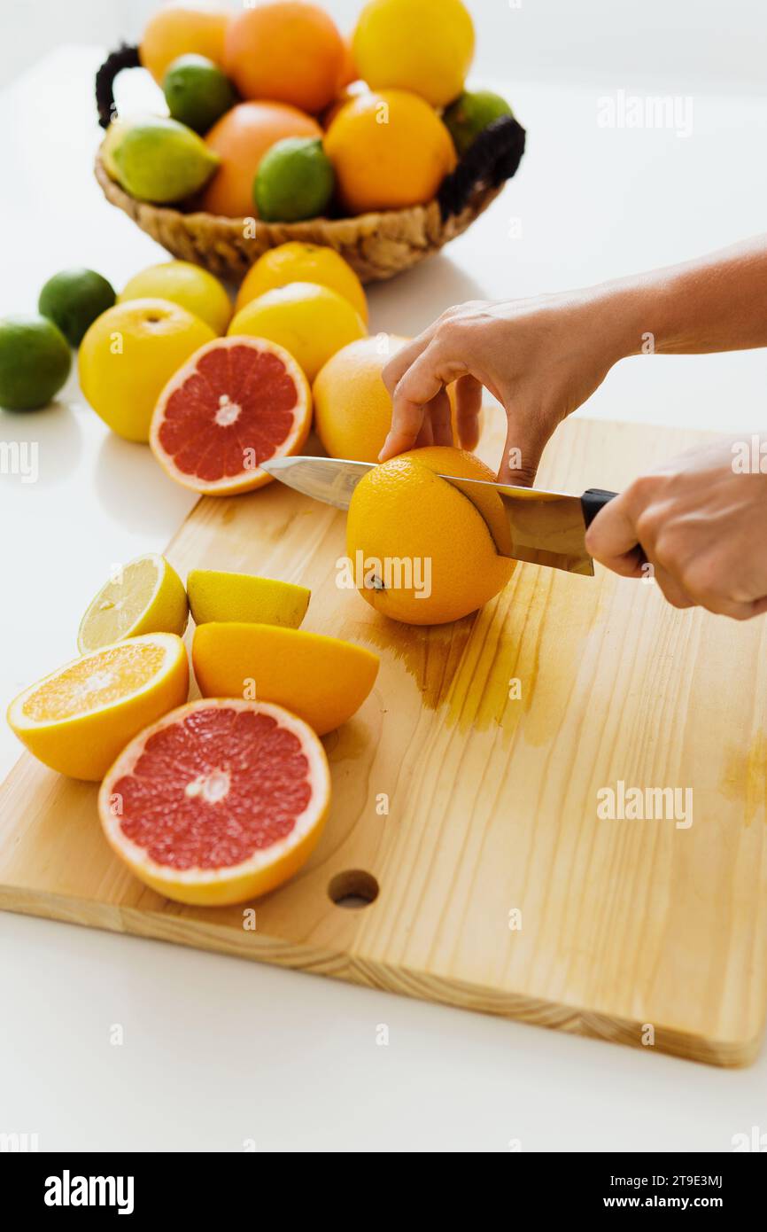 Großaufnahme von weiblichen Händen mit Messer, das Zitrusfrüchte auf Schneidebrett für hausgemachten frischen Saft schneidet Stockfoto