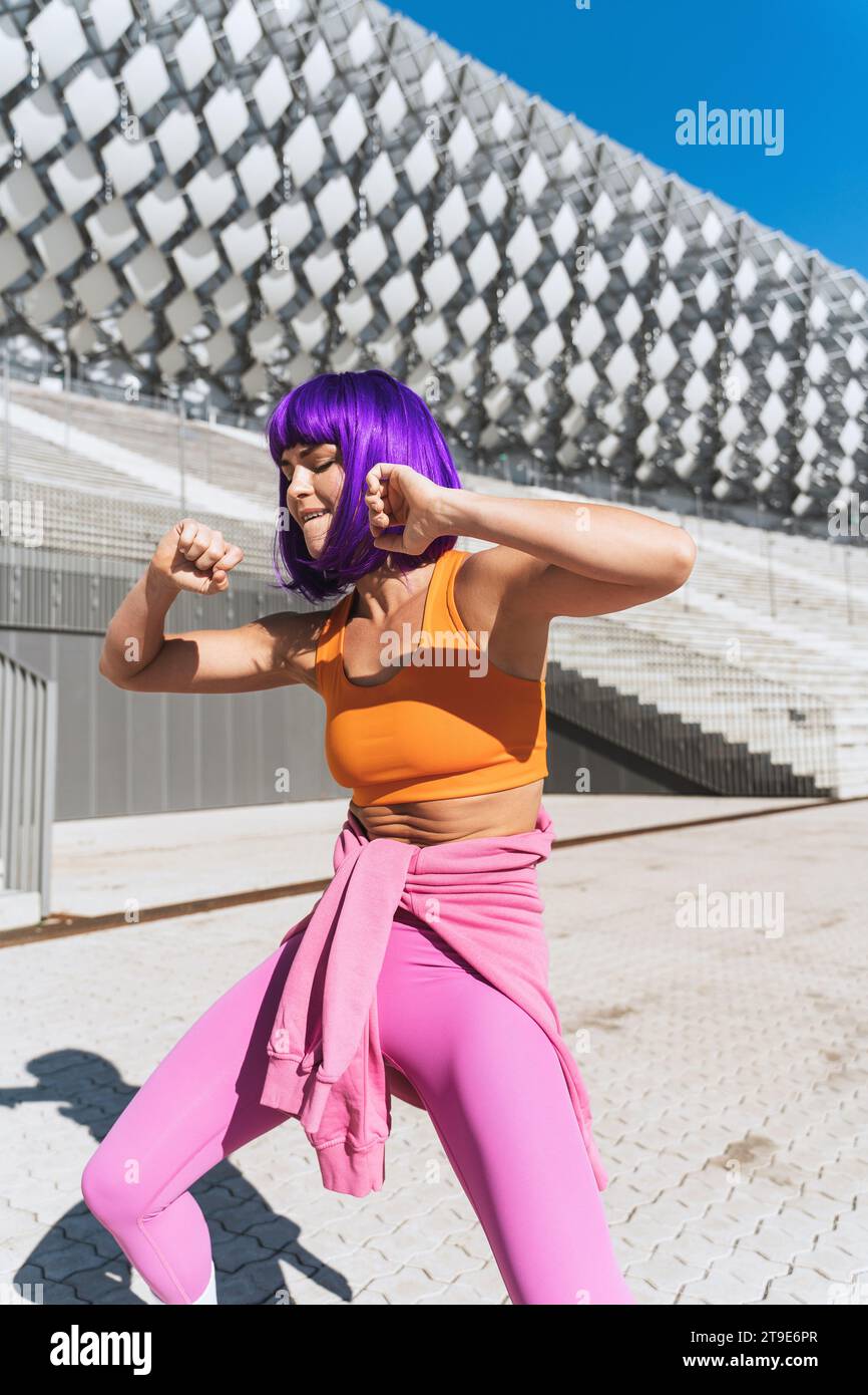 Sorglose aktive Tänzerin in farbenfroher Sportkleidung, die sich an sonnigen Tagen auf der Straße amüsiert Stockfoto