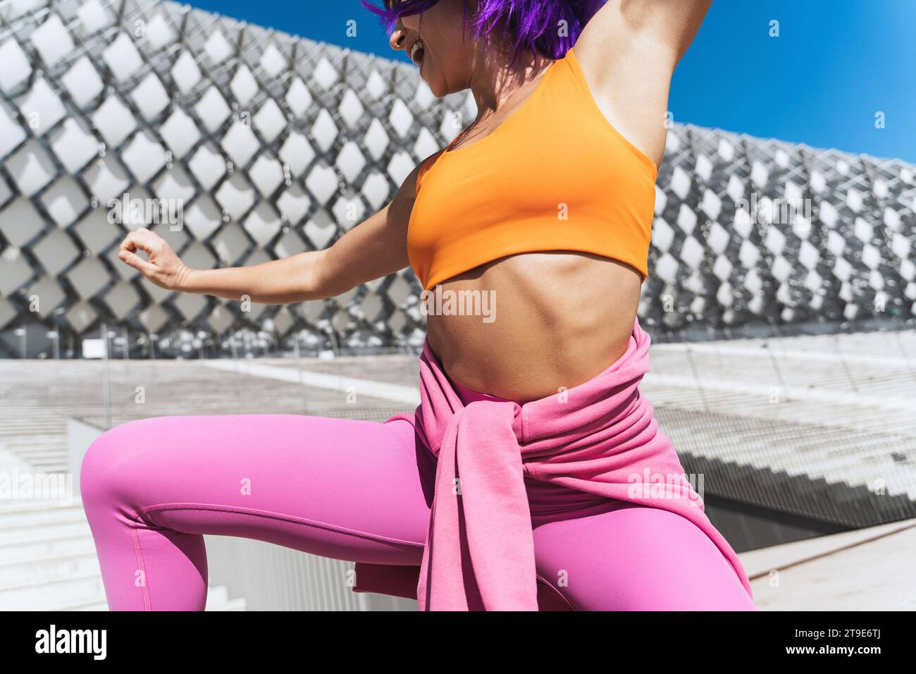 Sorglose aktive Tänzerin in farbenfroher Sportkleidung, die sich an sonnigen Tagen auf der Straße amüsiert Stockfoto