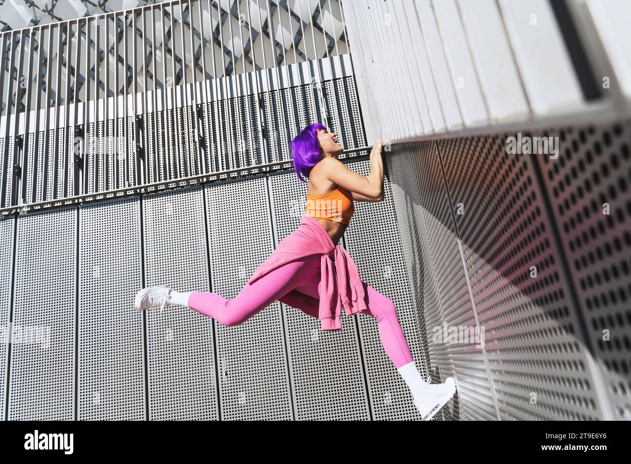 Glückliche aktive Frau in farbenfroher Sportkleidung, die an der Wand klettert Stockfoto