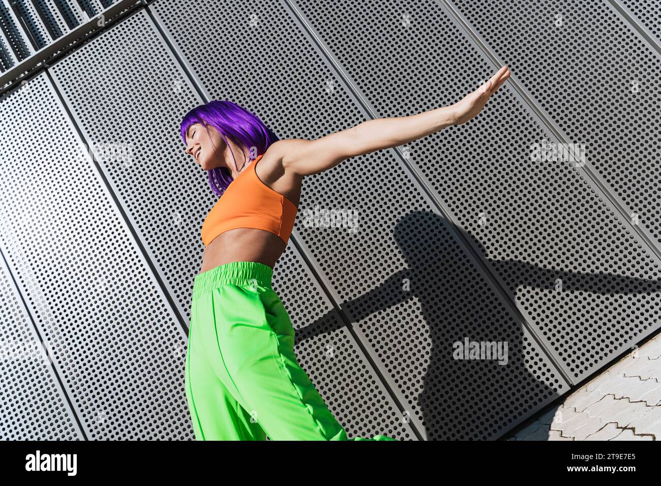 Sorglose aktive Tänzerin in farbenfroher Sportkleidung, die sich an sonnigen Sommertagen auf der Straße amüsiert Stockfoto