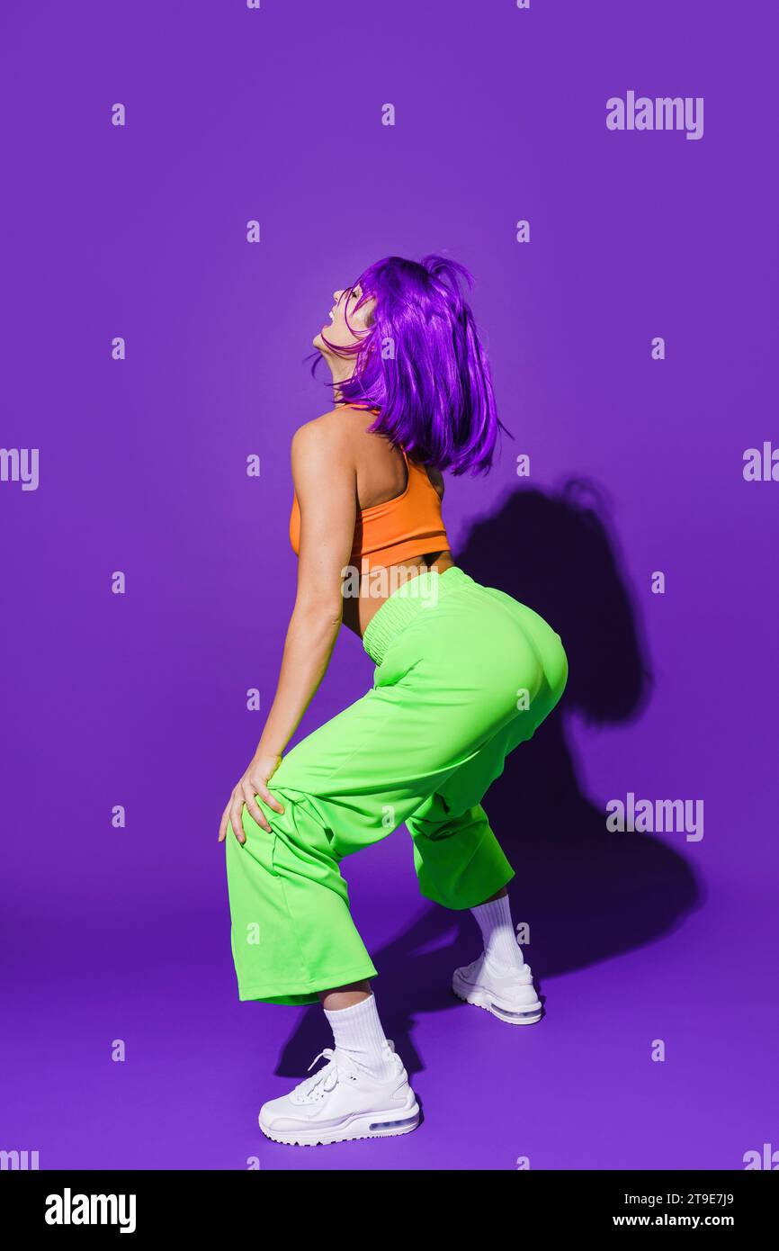 Sorglose Tänzerin in farbenfroher Sportswear-Twerking vor violettem Hintergrund Stockfoto