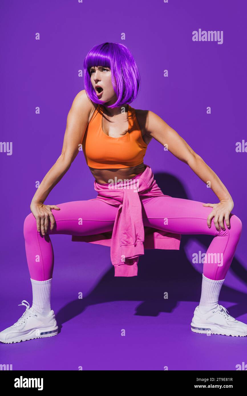 Sorglose junge Tänzerin in farbenfroher Sportkleidung, die vor purpurrotem Hintergrund auftritt Stockfoto