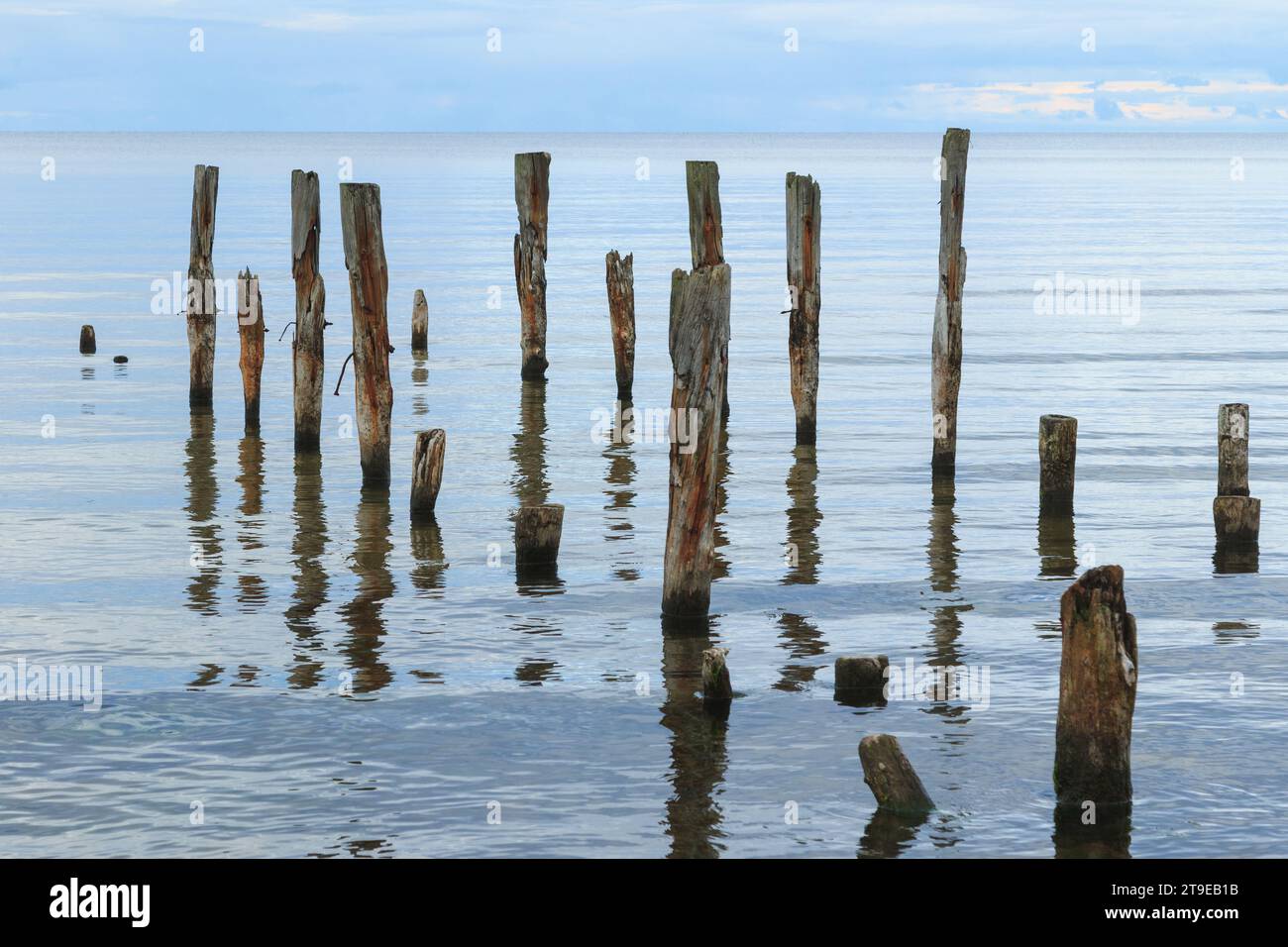 Eine wunderschöne Aufnahme einer ruhigen Meereslandschaft mit gebrochenen Pier-Pfählen, die aus dem Wasser ragen, auf dem Horizont. Stockfoto