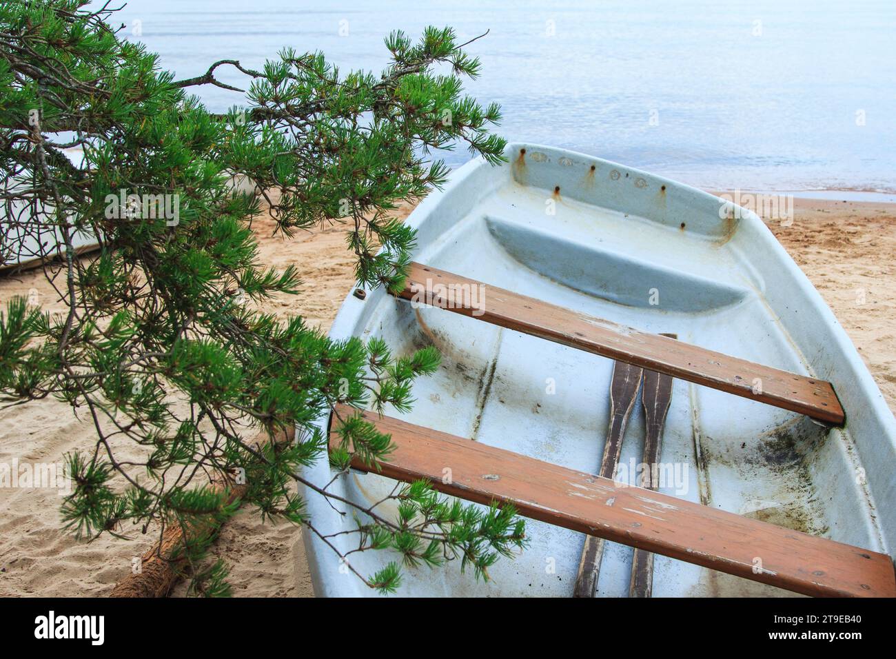 Nahaufnahme eines verlassenen schäbigen Fischerbootes, das an einem Sandstrand in der Nähe des ruhigen Meerwassers liegt. Stockfoto