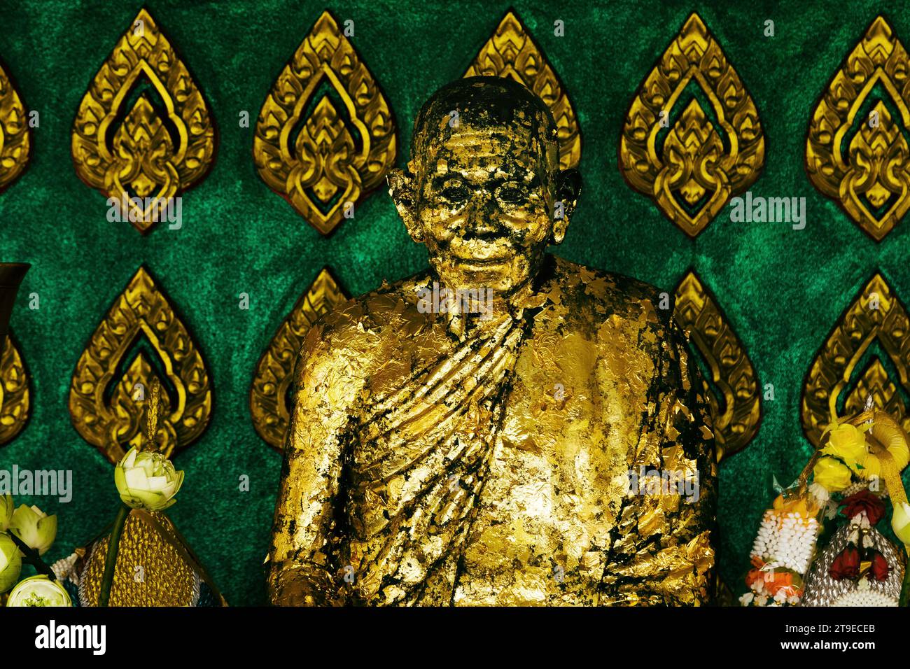 Nahaufnahme einer schäbigen, betenden buddhistischen Mönchsstatue, die mit goldener Farbe bedeckt ist. Stockfoto