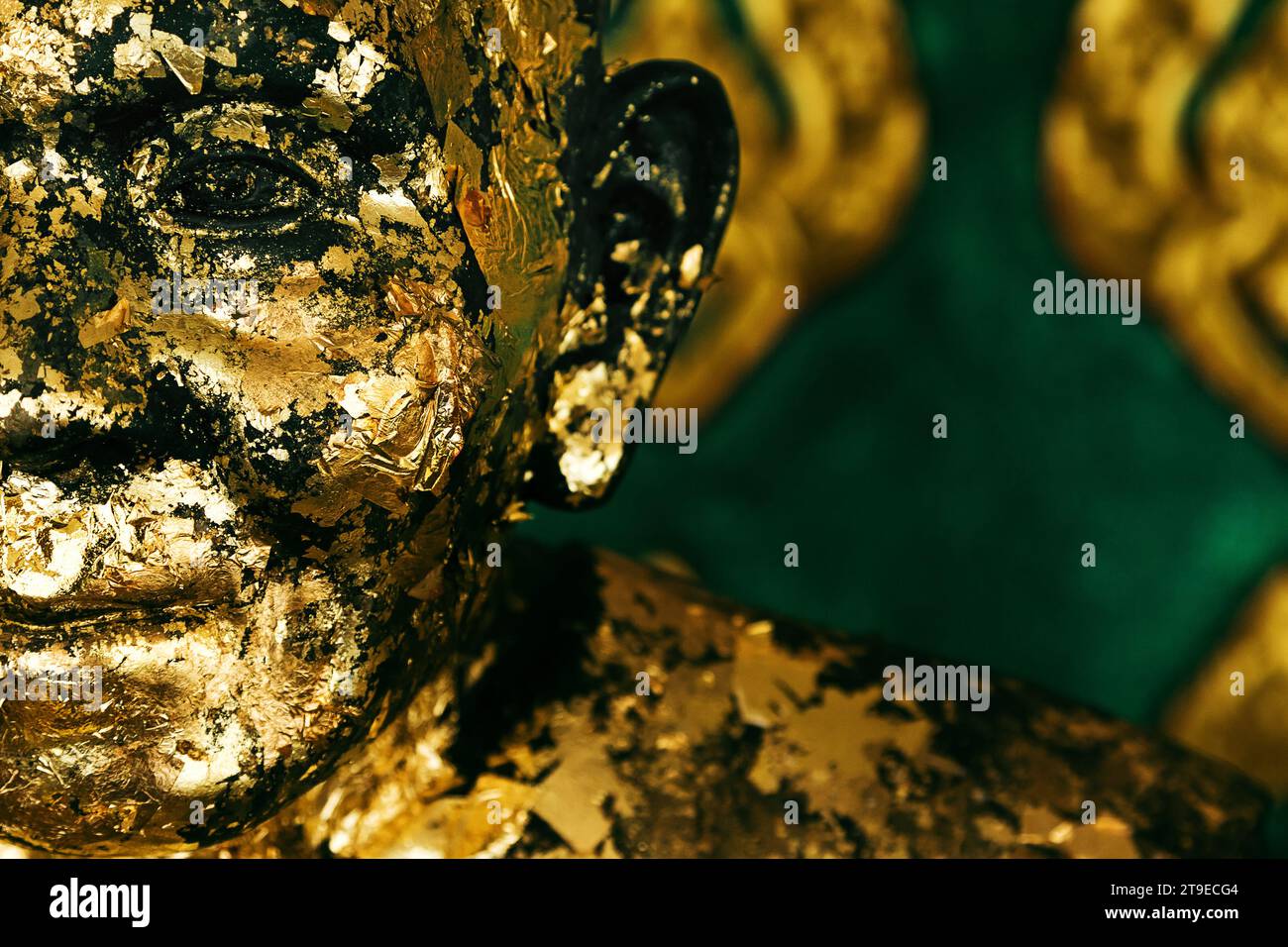 Nahaufnahme einer schäbigen, betenden buddhistischen Mönchsstatue, die mit goldener Farbe bedeckt ist. Stockfoto