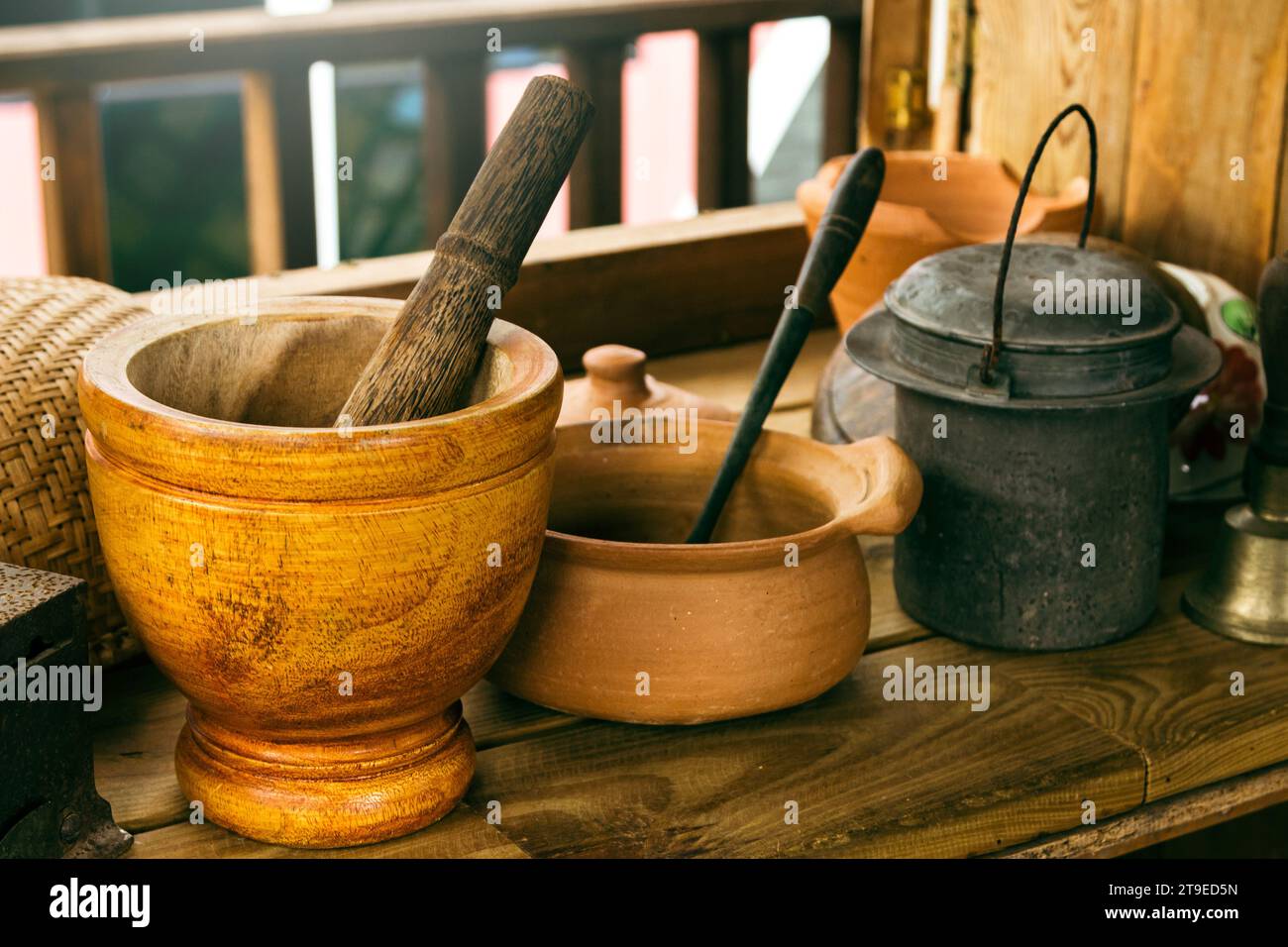 Nahaufnahme von handwerklich hergestelltem Mörtel, Stößel und anderem Küchengeschirr auf dem Holztisch im Landhaus. Stockfoto