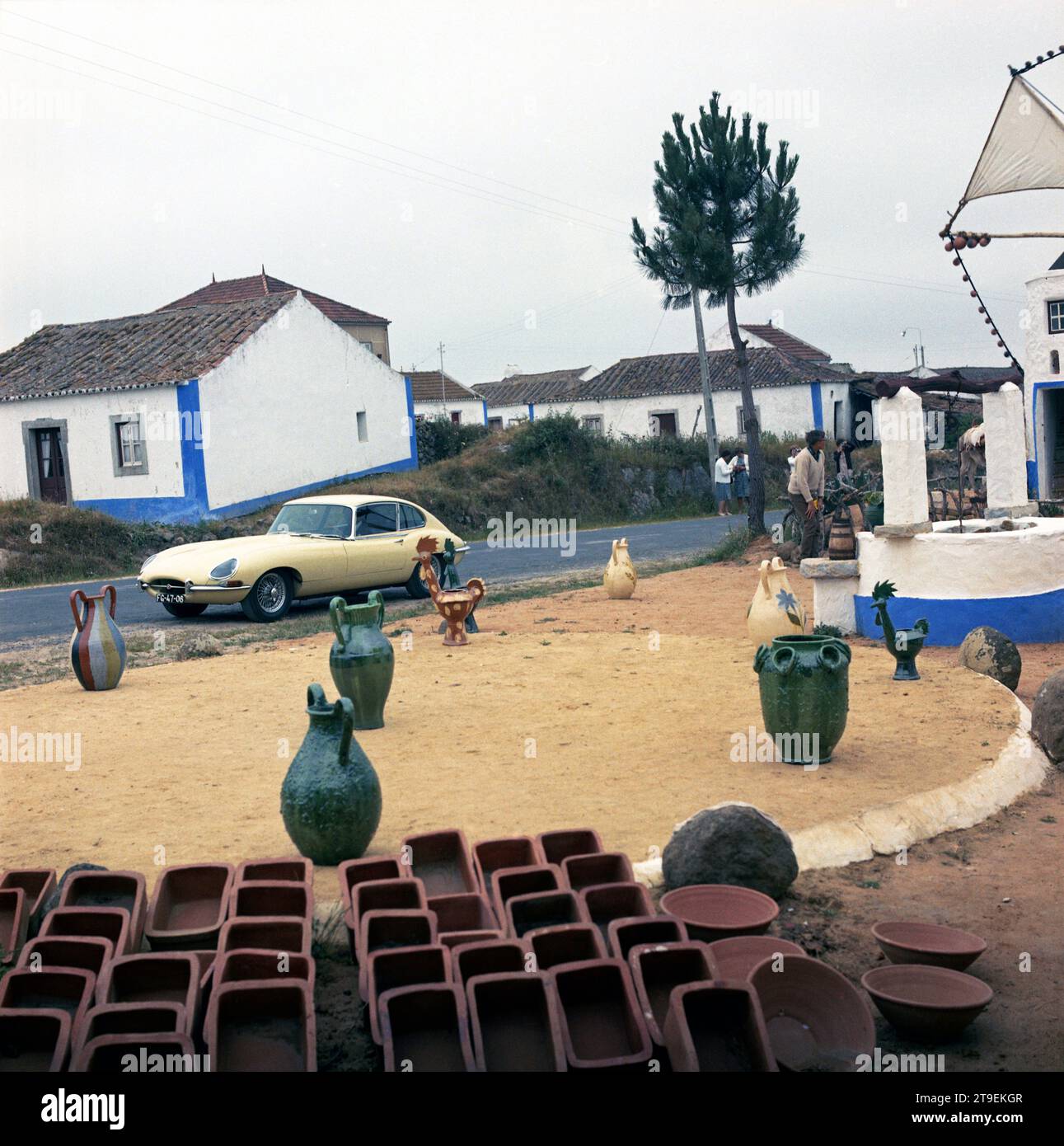 1966 Creme Jaguar E-TYPE, Serie 1, 2+2, in portugiesischem Küstendorf mit blau-weiß getünchten Häusern, Brunnen, Windmühle und Keramik Stockfoto