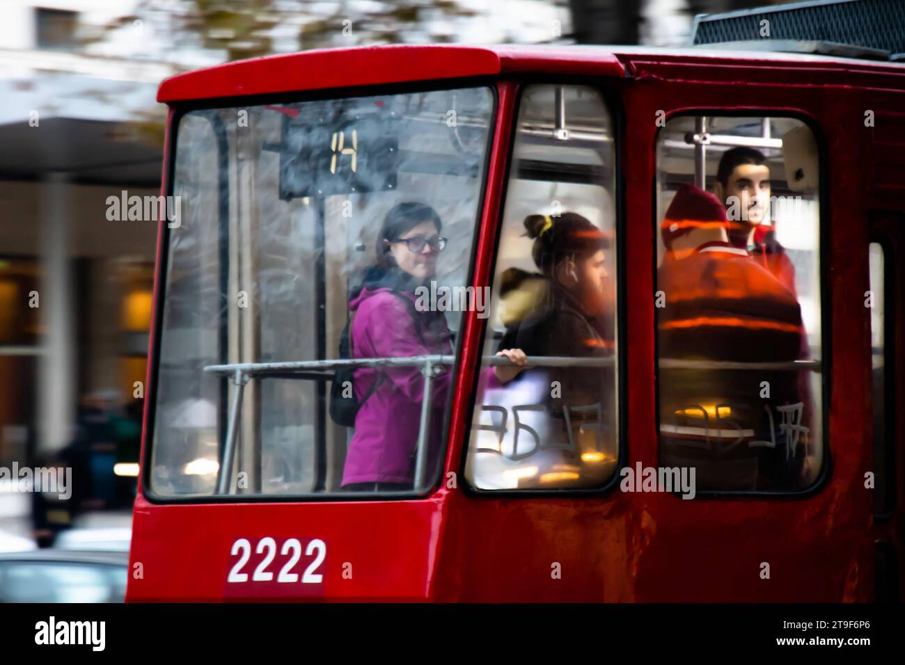Belgrad, Serbien, 23. November 2023: Jugendliche, die in einer roten Straßenbahn Nr. 14 mit Graffiti und Reflexionen durch das Fenster fahren Stockfoto