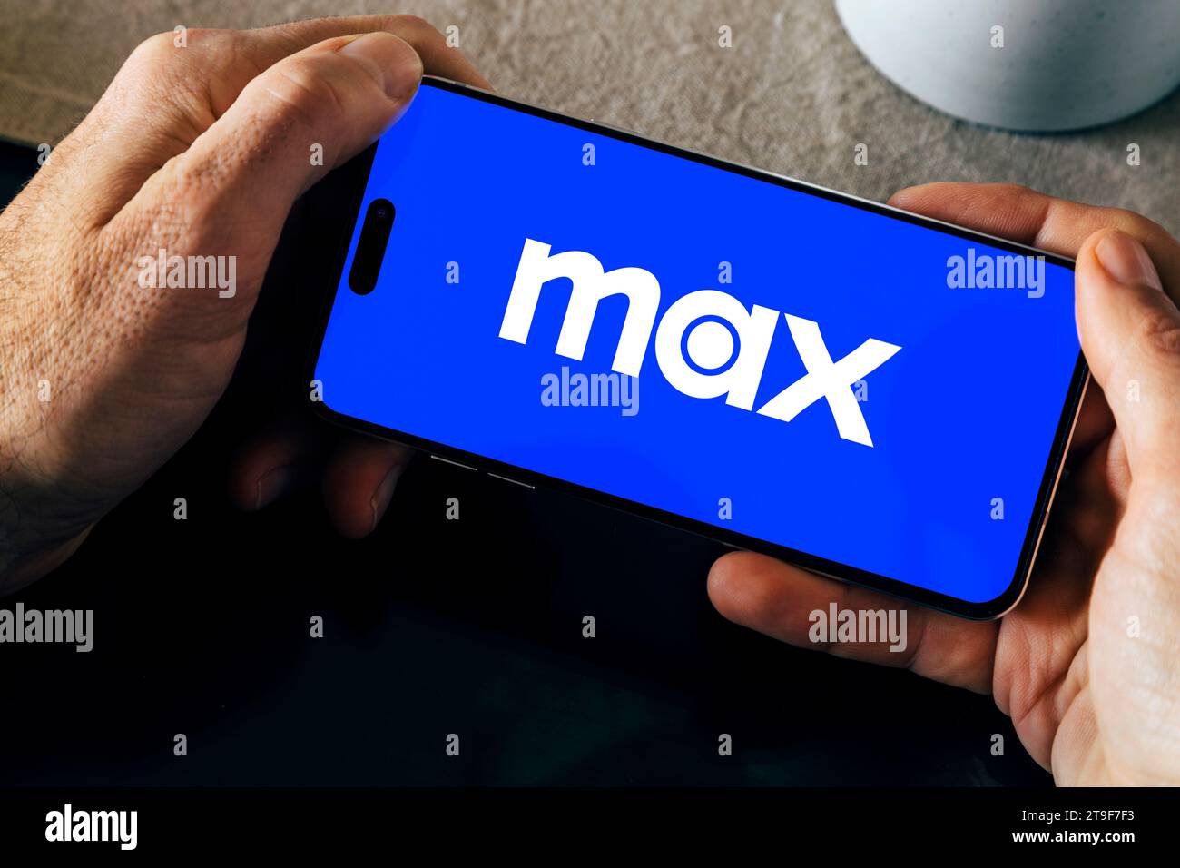 HBO Max Logo auf dem Handy-Bildschirm auf einem Tisch. Mann, der ein Smartphone hält, während die App geöffnet ist. Rosario, Argentinien - 23. November 2023. Stockfoto