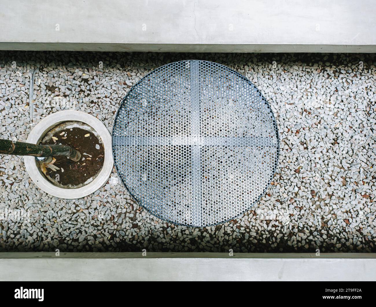 Runder Metalltisch in der Mitte des Kiesgartens neben einem Baum, umgeben von langen Betonsitzen. Modernes Außendesign. Flache Lagen oder Draufsicht. Stockfoto