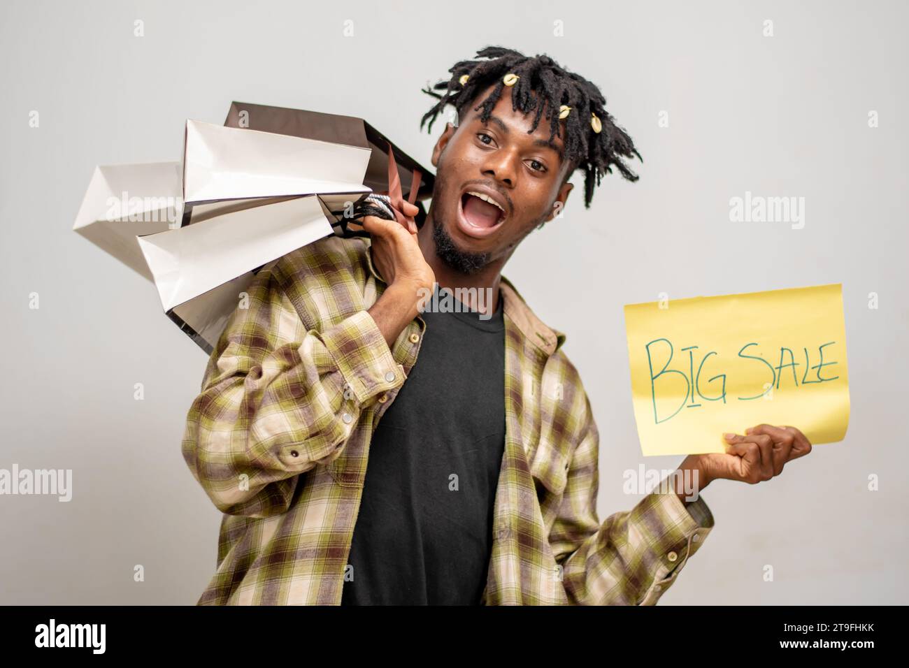 Überraschter afrikanischer, gutaussehender Mann mit Einkaufstasche und gelber Karte mit Big Sale-Aufschrift. Black Friday Stockfoto