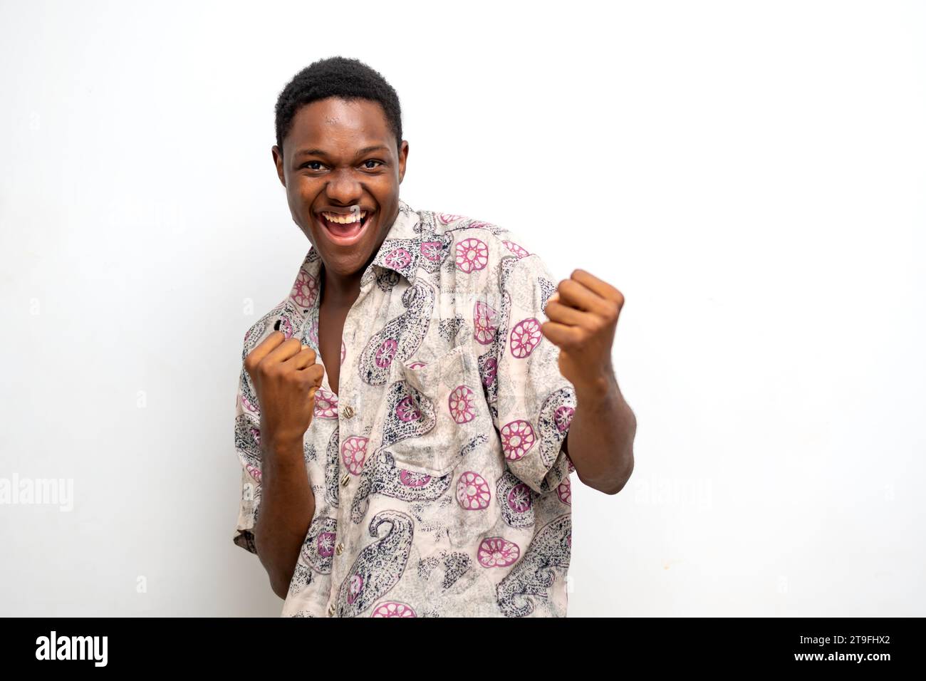 Überregter junger Schwarzer, der die Faust auf weißem Hintergrund hochhebt und den Erfolg feiert. Glücklicher afrikanischer Millennial-Mann, der positive Emotionen teilt, Copy Spa Stockfoto