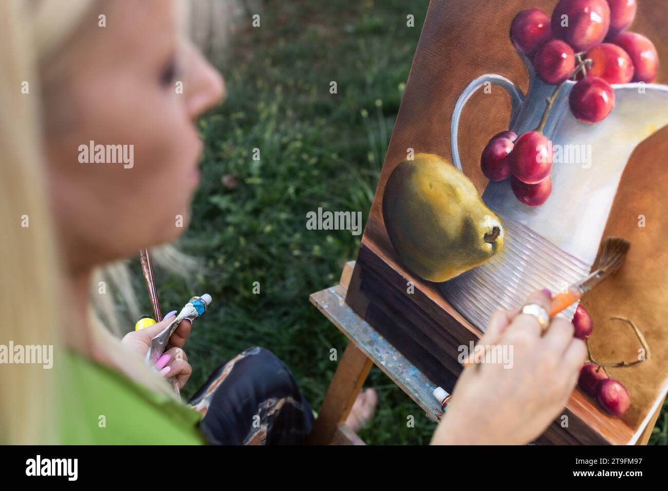 Nahaufnahme einer jungen, blonden Frau, die im Freien tote Natur auf Leinwand malt Stockfoto