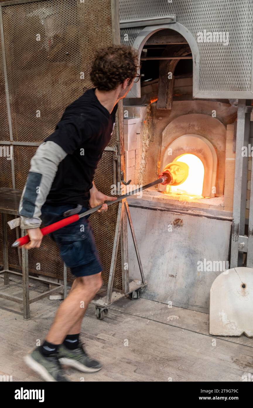 Eine große Vase aus klarem Glas, die von einem Glasbläser mit einem 2 m langen Ionenstab, genannt Punty oder Pontil, in einem der Funances erhitzt wird Stockfoto