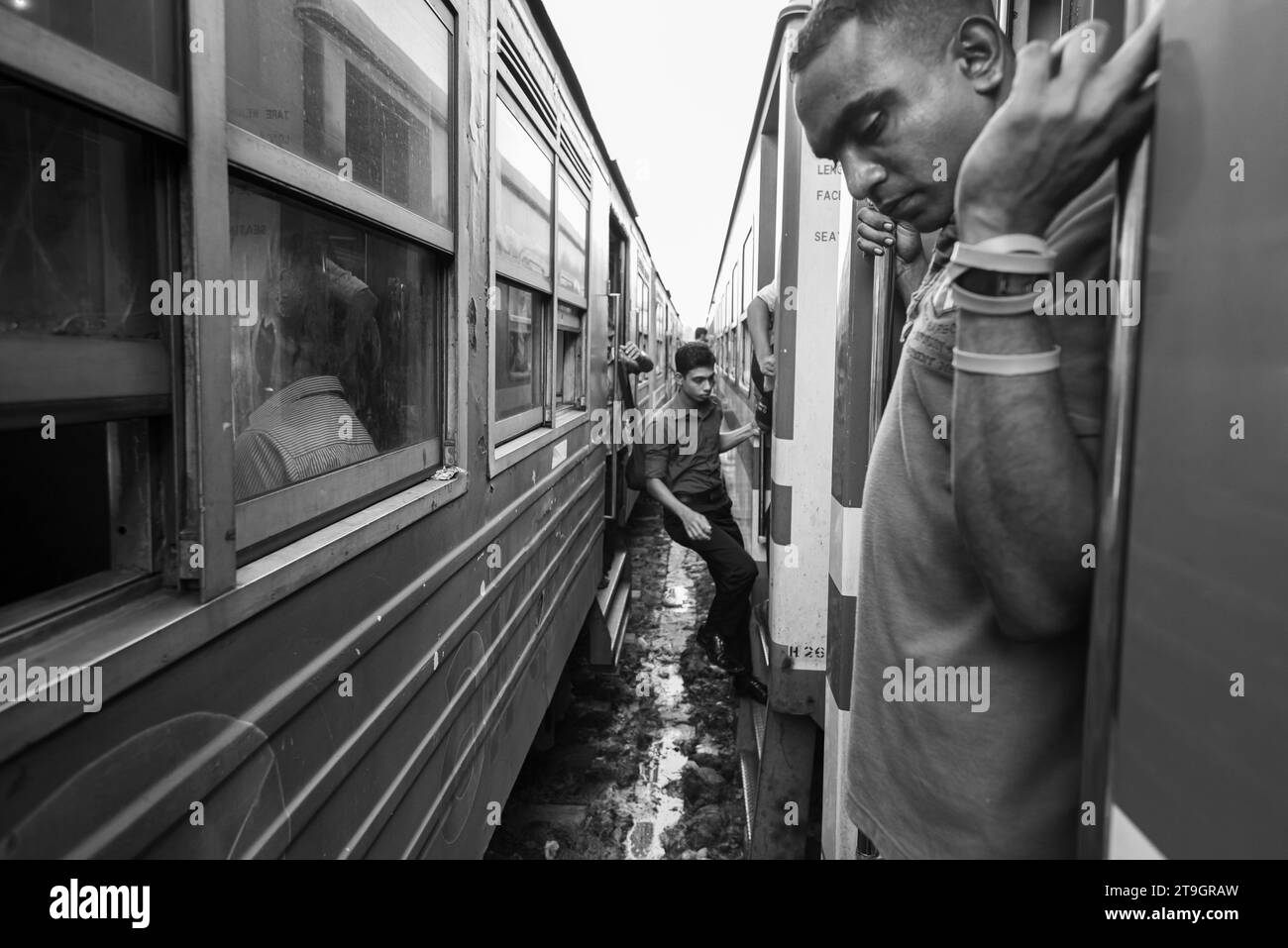 Ein Mann hängt an der Außenseite eines Zuges, während ein anderer an einem Bahnhof in Sri Lanka von einem Zug zum anderen wechselt Stockfoto