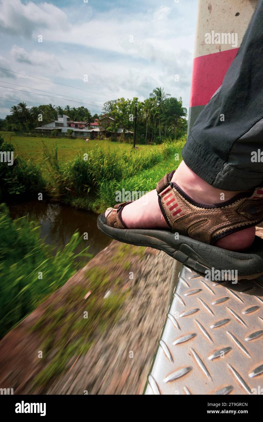 Ein bemannter Fuß mit Sandalen ruht an der Tür eines fahrenden Zuges in Sri Lanka Stockfoto