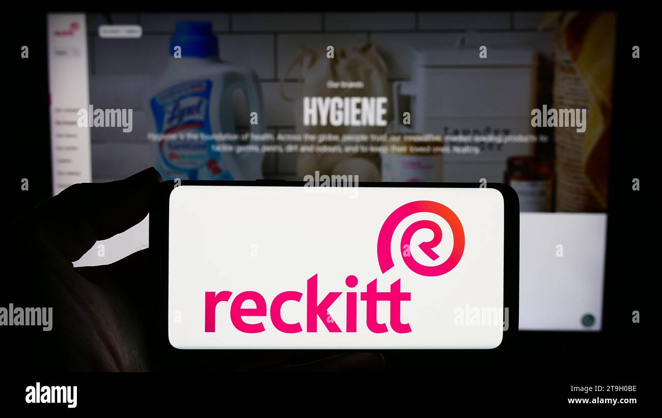 Person mit Smartphone und Logo des Konsumgüterunternehmens Reckitt Benckiser Group plc vor der Website. Schwerpunkt auf dem Display des Telefons. Stockfoto