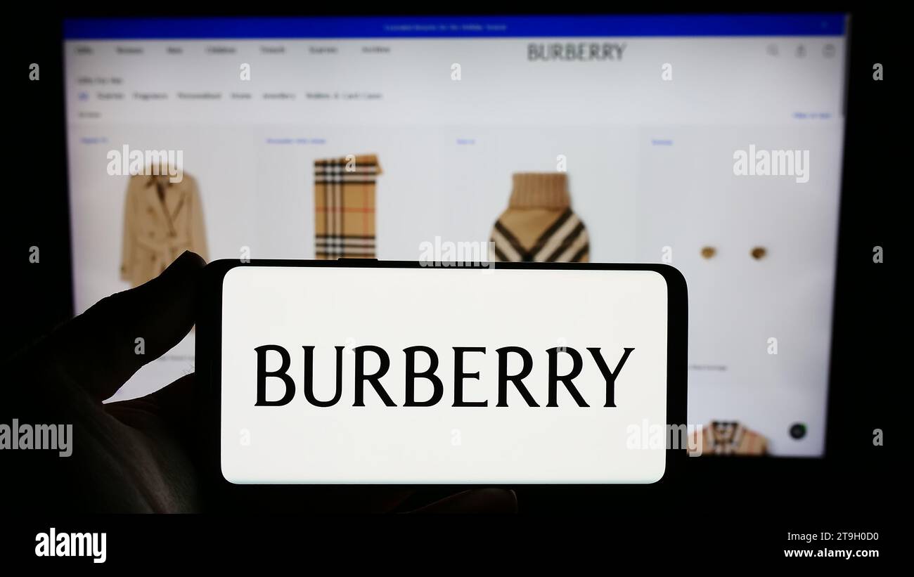 Person mit Smartphone und Logo des britischen Luxusmodeunternehmens Burberry Group plc vor der Website. Schwerpunkt auf dem Display des Telefons. Stockfoto